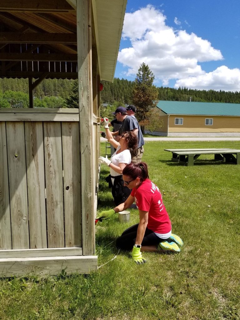 Volunteers painting a wooden building exterior on a sunny day, participating in community service to improve local infrastructure.