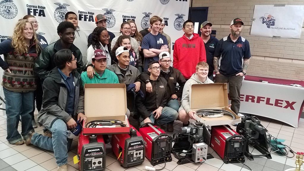 Group photo of students and instructors with welding equipment and FFA banner, highlighting a vocational training session.