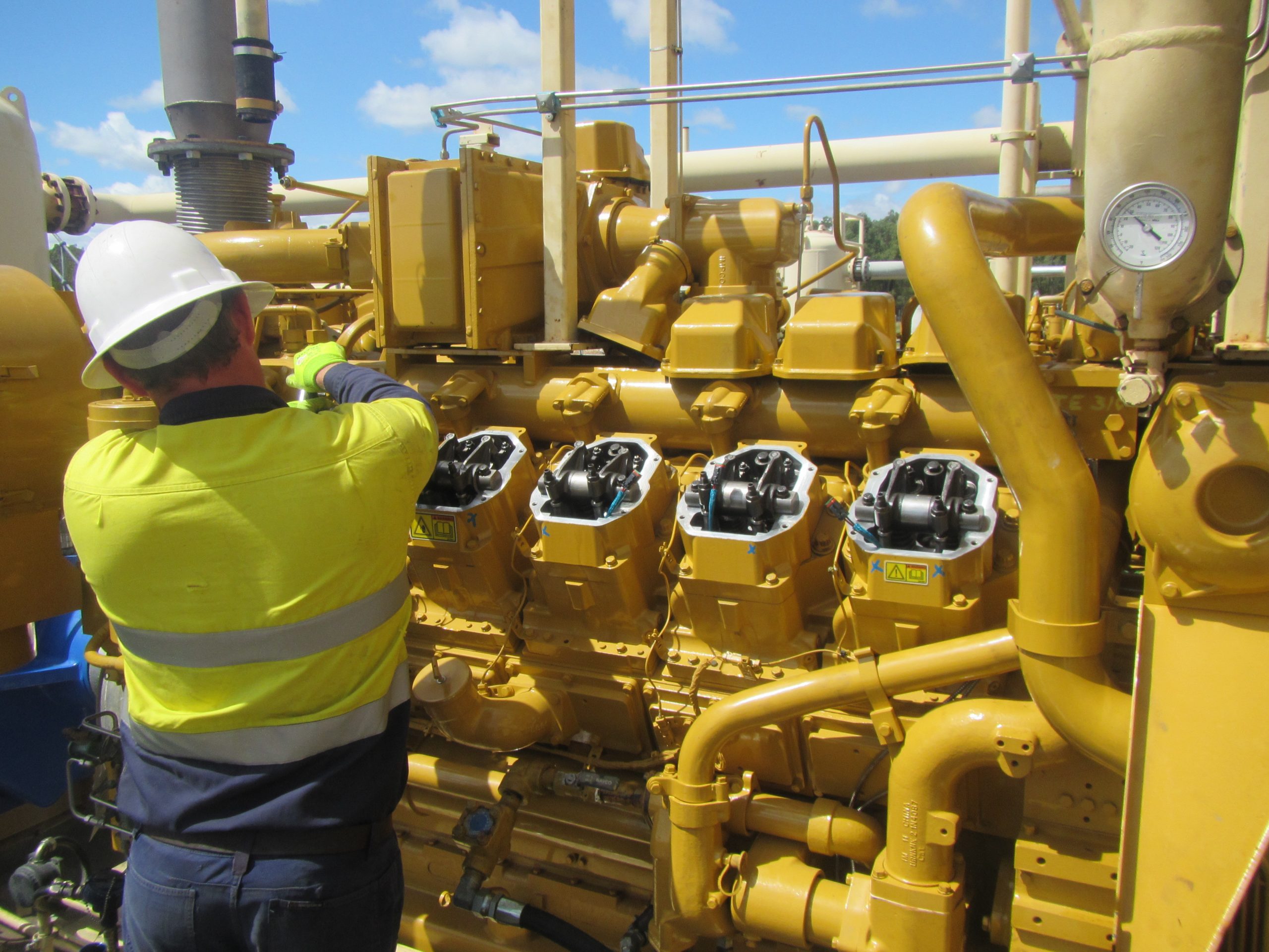 Worker in a safety helmet and high-visibility vest maintaining a large industrial engine outdoors.