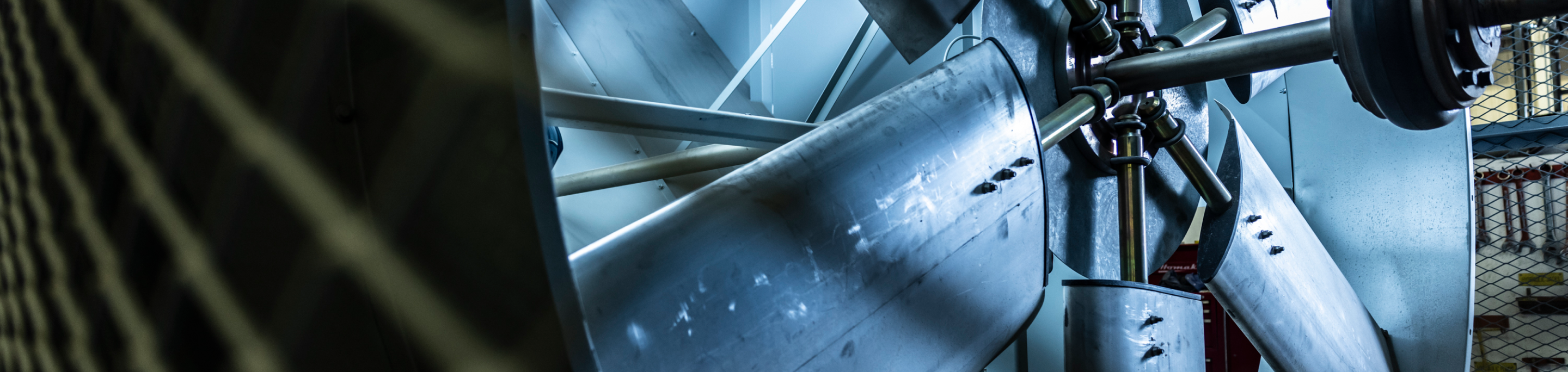 Close-up of a large industrial metal fan blade in a manufacturing facility, emphasizing the details of its structure.