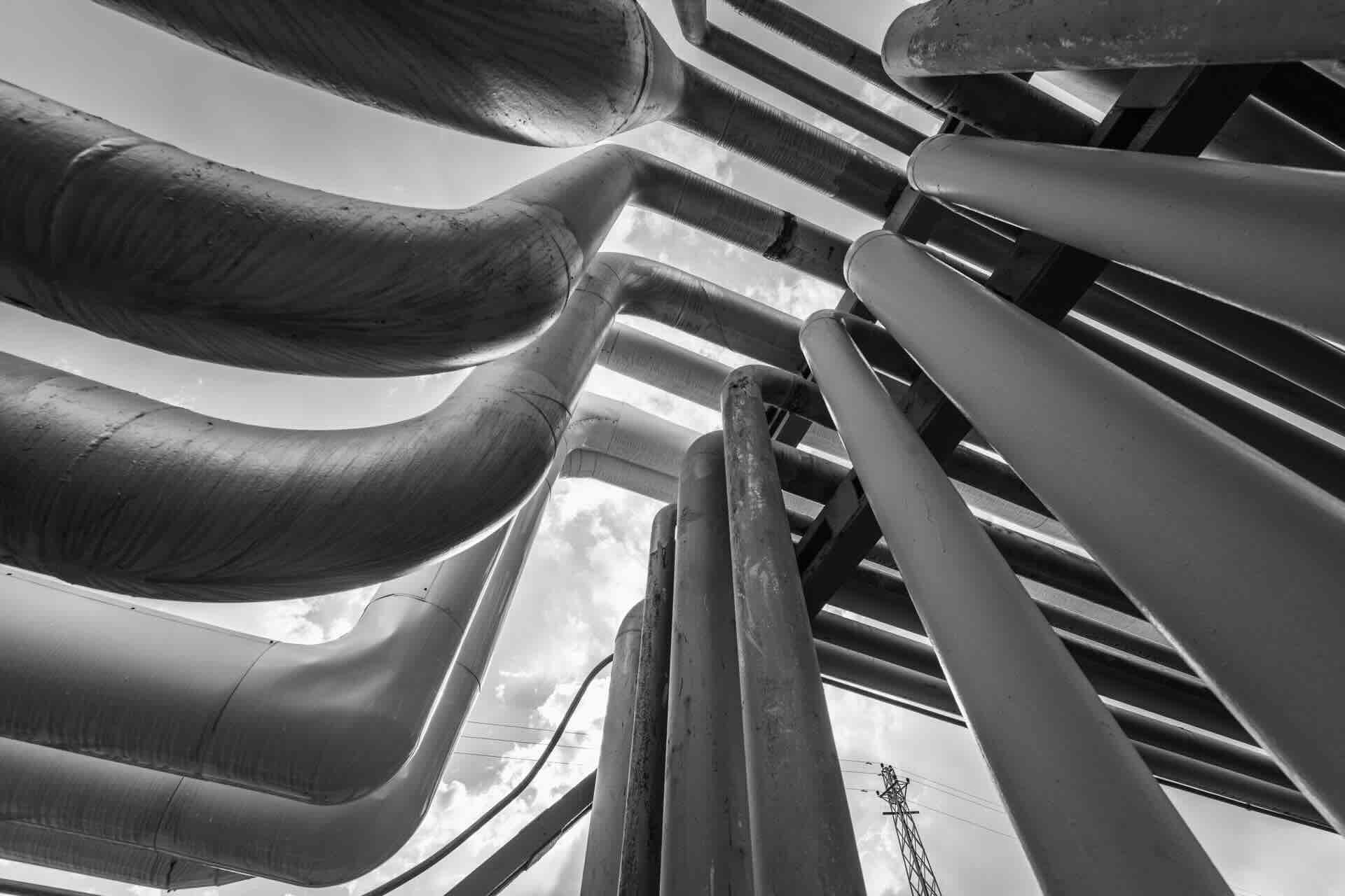 Black and white photo of large industrial pipes intertwining against a cloudy sky, emphasizing engineering and construction.