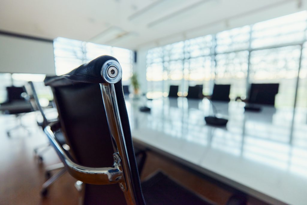 A sleek, empty boardroom with chrome and black seating and a long bay of windows