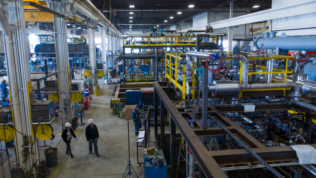 A photo of the inside of an Enerflex facility, with two hardhatted employees walking