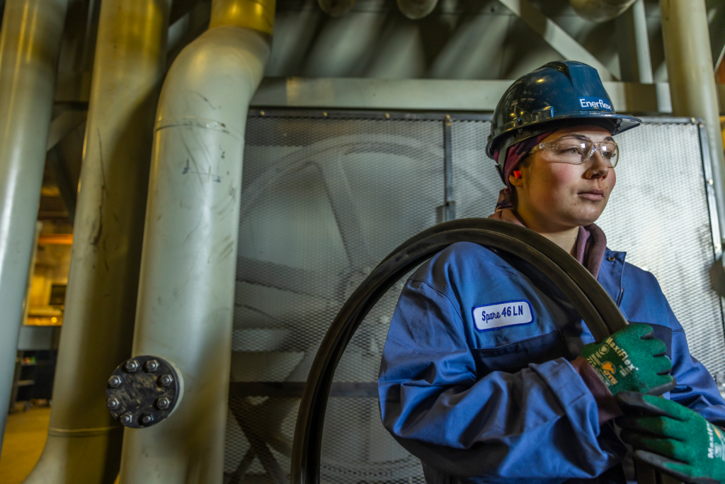 Female industrial worker in safety gear holding a pipe in a factory setting, demonstrating focus and determination.